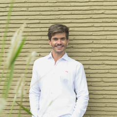 Hombre con camisa blanca sonriendo sobre fondo de ladrillo