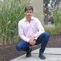 Hombre con camisa rosada, jeans y botas negras en exterior.