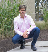 Hombre con camisa rosada, jeans y botas negras en exterior.